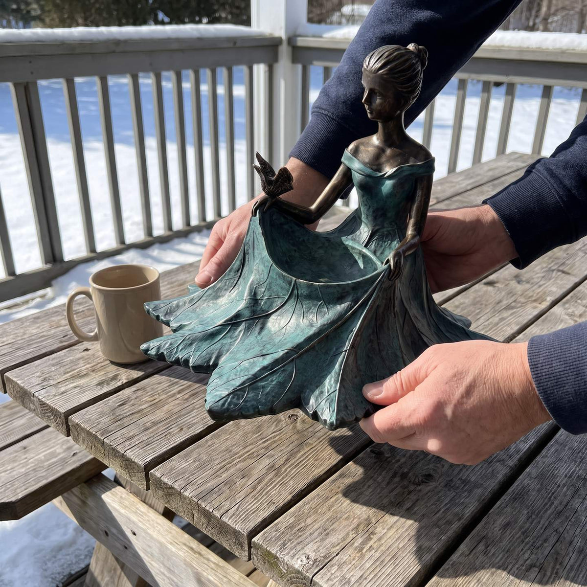 Two hands lifting the bird bath, a coffee mug for scale