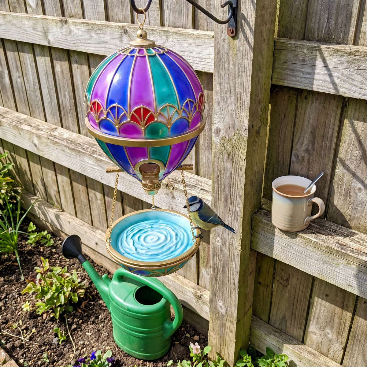 Balloon bird feeder on a fence post with watering can and mug for size