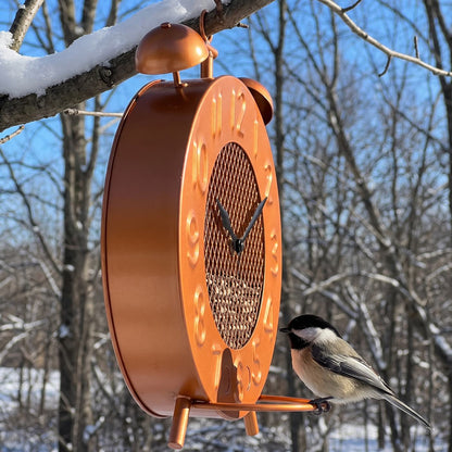 Side view of the copper clock bird feeder hanging from a branch with a chickadee