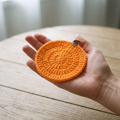 A single pumpkin coaster held flat in an open palm, showing its true 4-inch size
