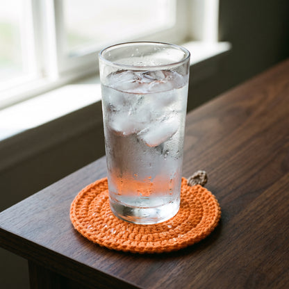 A sweating glass of iced water on a pumpkin coaster with the surrounding wood staying dry