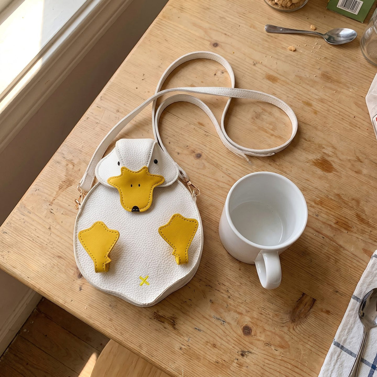 Delphine's white duck crossbody bag lying on a kitchen table next to a coffee mug