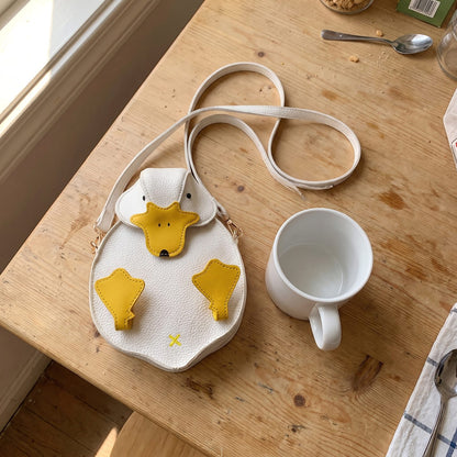 Delphine's white duck crossbody bag lying on a kitchen table next to a coffee mug