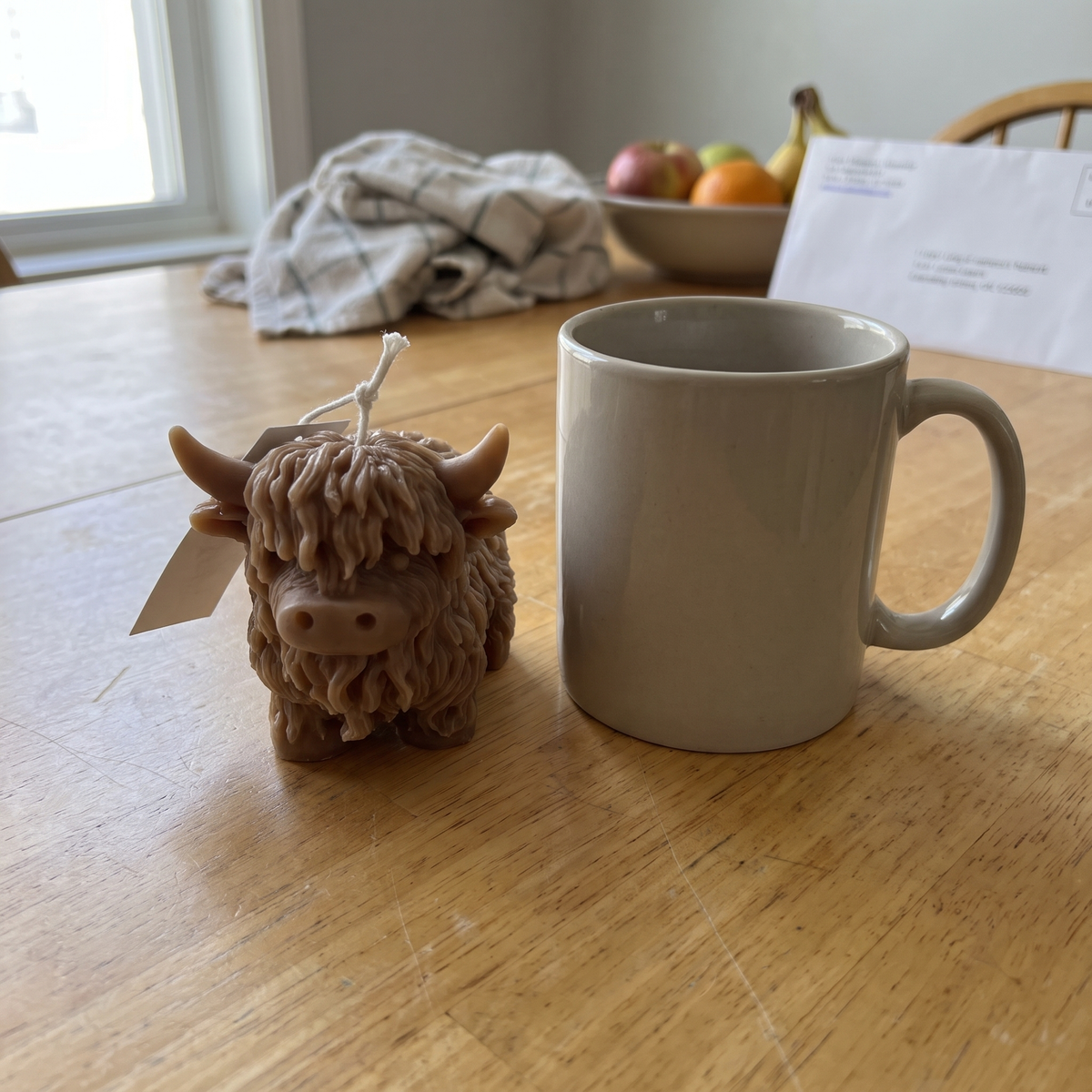 Brown Highland Cow candle next to a coffee mug
