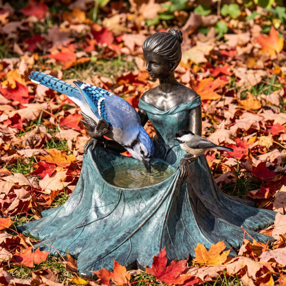 Bronze bird bath among red maple leaves with a blue jay drinking
