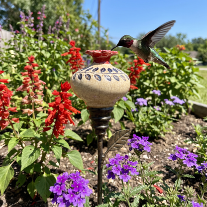 Dessie's hummingbird feeder with a hummingbird in a flower bed