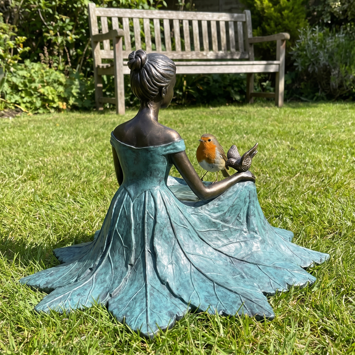 Back view of the bronze girl with a robin at the bowl, garden bench behind