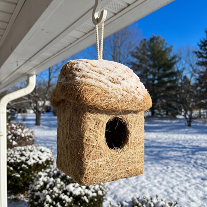 Coconut fiber roosting hut hanging under a snowy porch eave