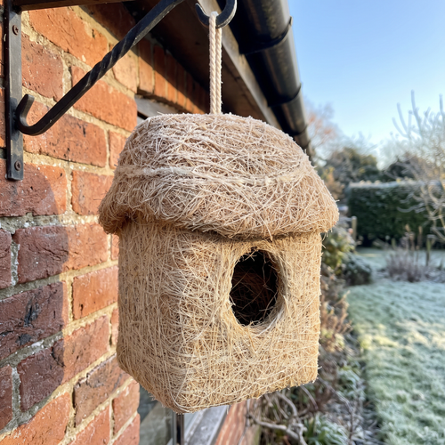 Coconut fibre roosting hut hanging under the eave of a brick cottage