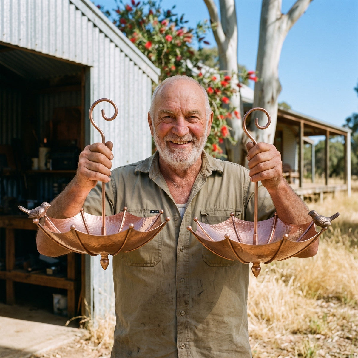 Kelvin Treloar holding two of his copper umbrella bird baths outside his shed