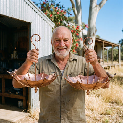 Kelvin Treloar holding two of his copper umbrella bird baths outside his shed