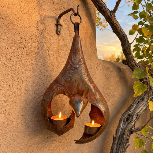 Tomás's iron bat lantern glowing on an adobe wall at dusk
