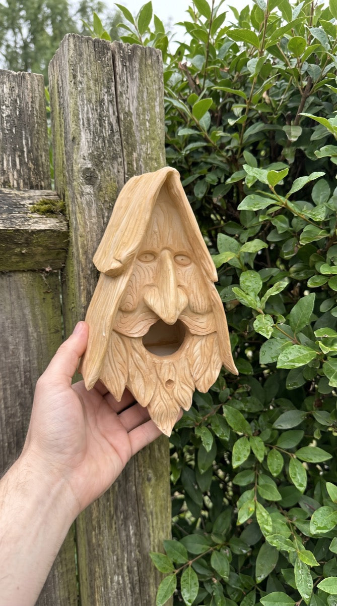 Wood-spirit birdhouse held by a garden fence