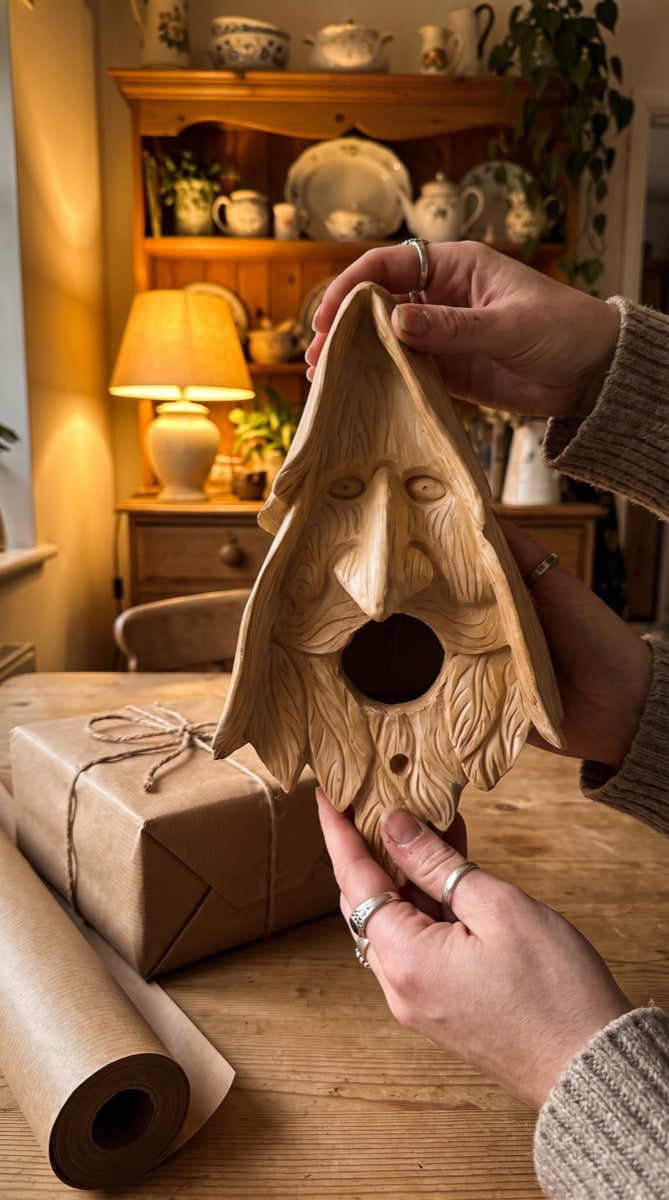 Wood-spirit birdhouse held indoors beside a wrapped gift