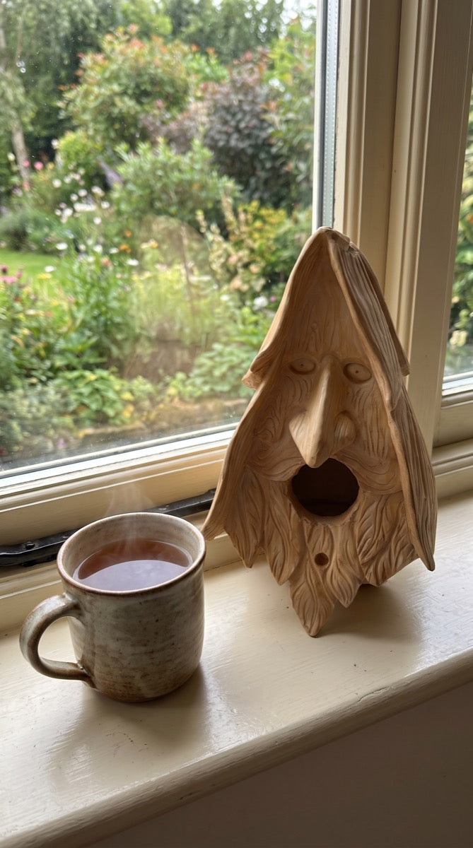 Wood-spirit birdhouse on a windowsill beside a mug of tea